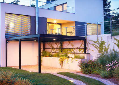 Metallcarport vor beleuchtetem Haus